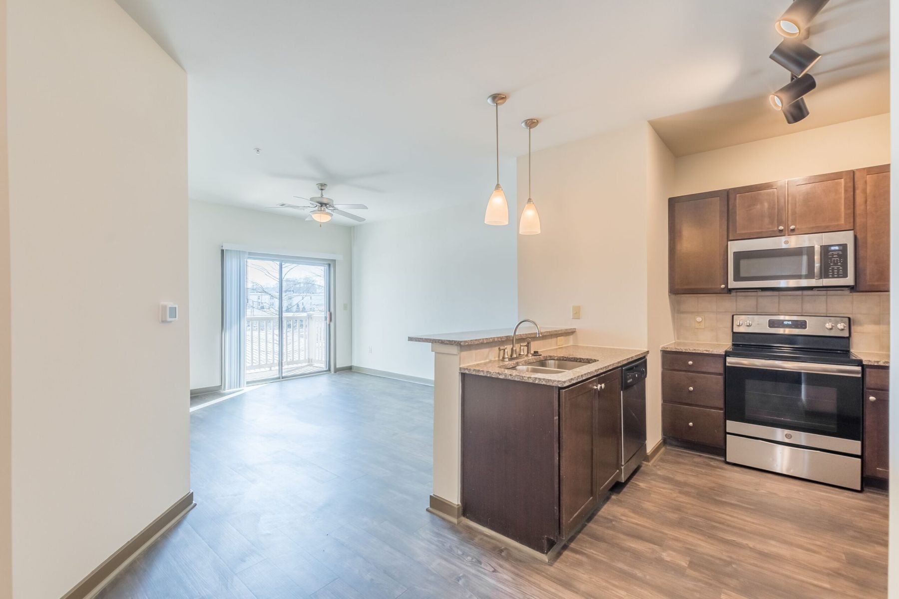 Empty room with wood floors, ceiling fan, and sliding glass door leading to a patio with vertical blinds at Apex West Midown.